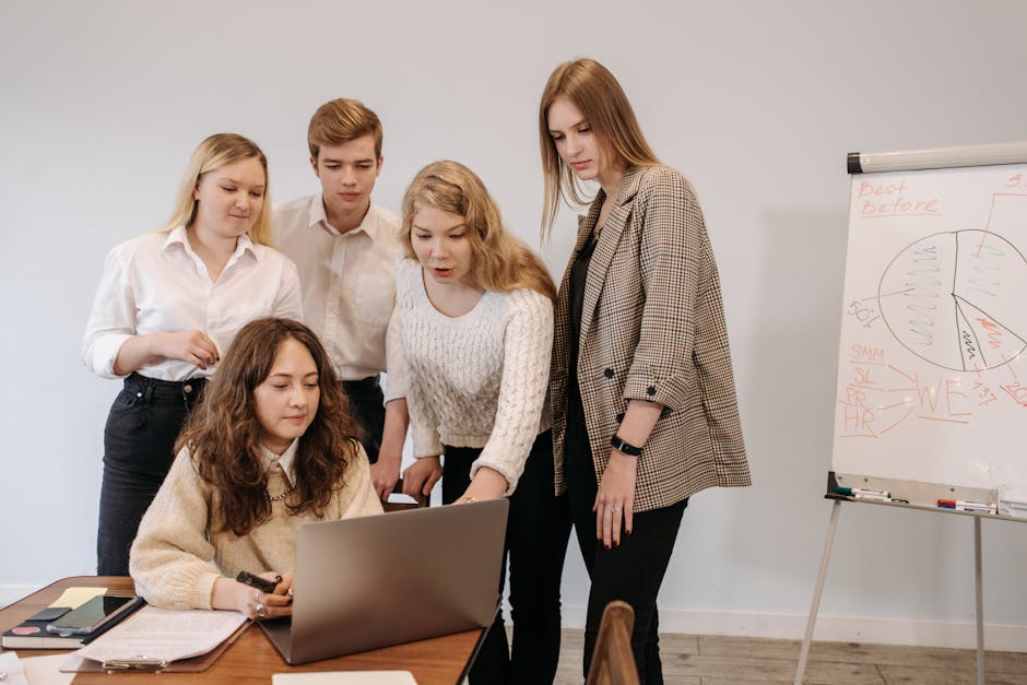 Group of young adults collaborating on a project with a laptop and whiteboard in a modern office setting
